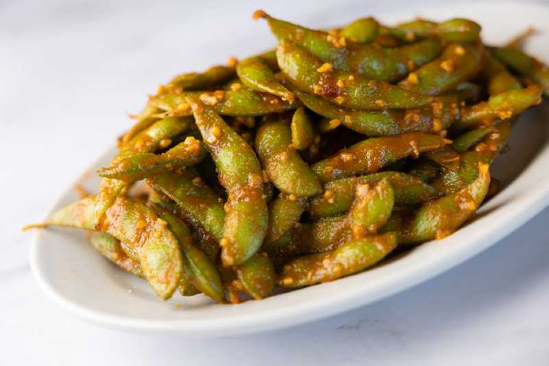 A bowl of spicy garlic edamame appetizer, coated in flavorful seasoning, a crowd favorite for those searching for Asian food near me or delicious starters at Sushi King Westside.