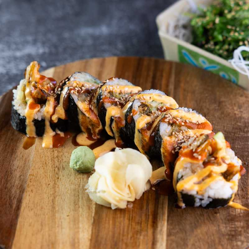 A New Mexican sushi roll on a wooden plate, topped with sauces and green chile, showcasing local flavors available at Sushi King and other sushi restaurants near me.