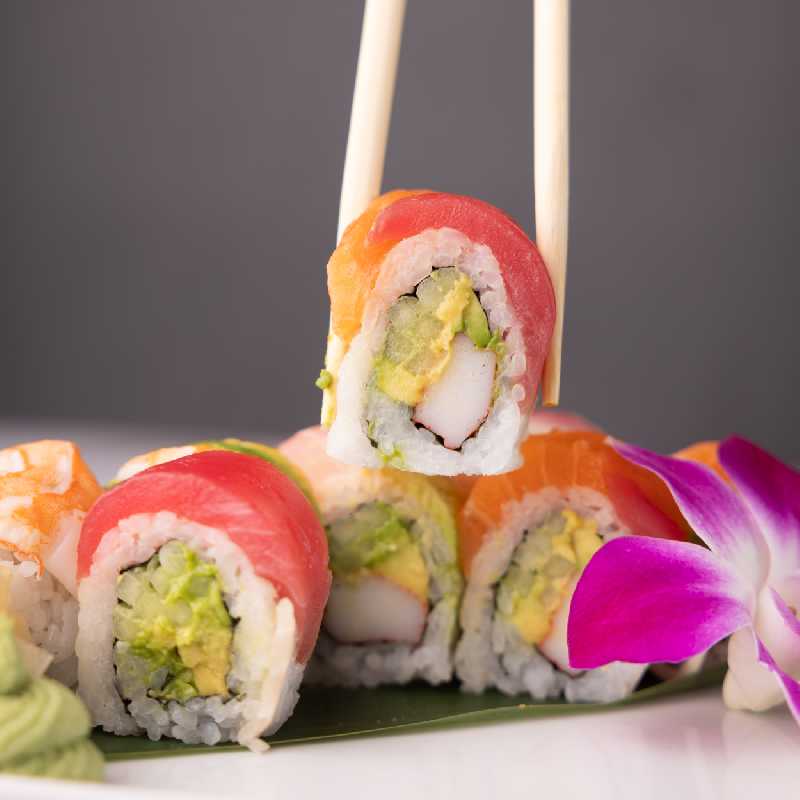 A rainbow sushi roll held with chopsticks, showcasing the artistry and taste of Sushi Albuquerque or Sushi Rio Rancho.